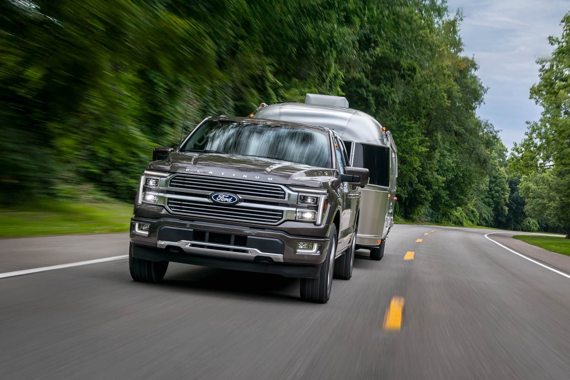 A gray Ford F-150 Platinum towing a silver travel trailer on a wooded road